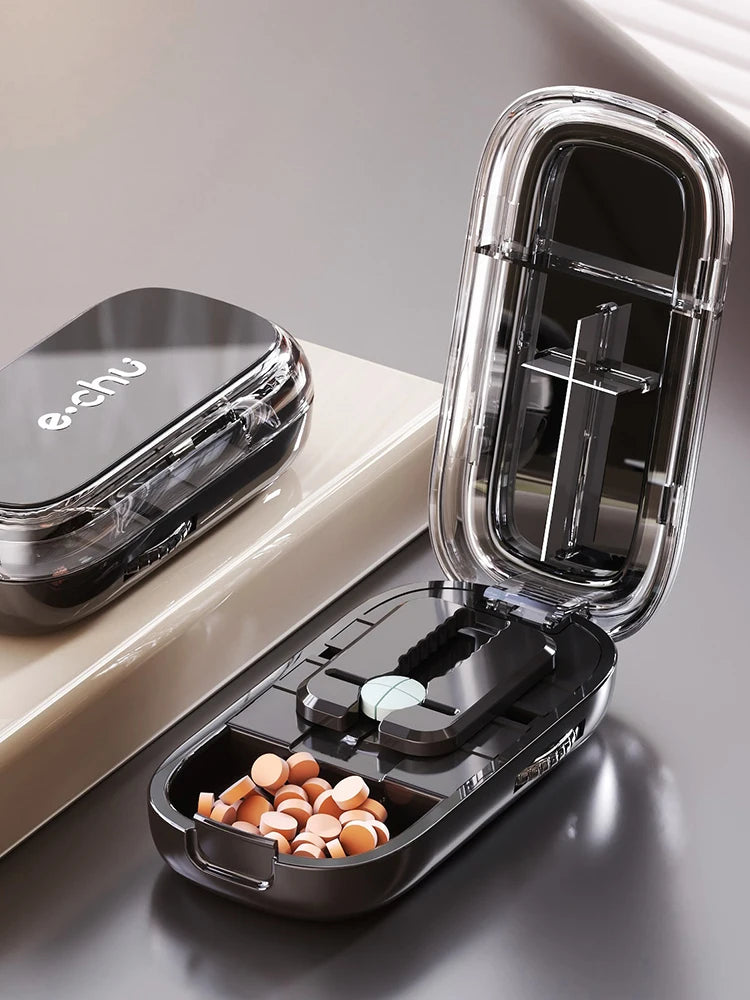 Beige and black Adjustable Pill Cutters by e.chu, one open with pills and one closed, on a beige surface with blinds in the background.