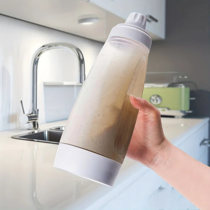Hand holding and shaking batter bottle mixer in a modern kitchen