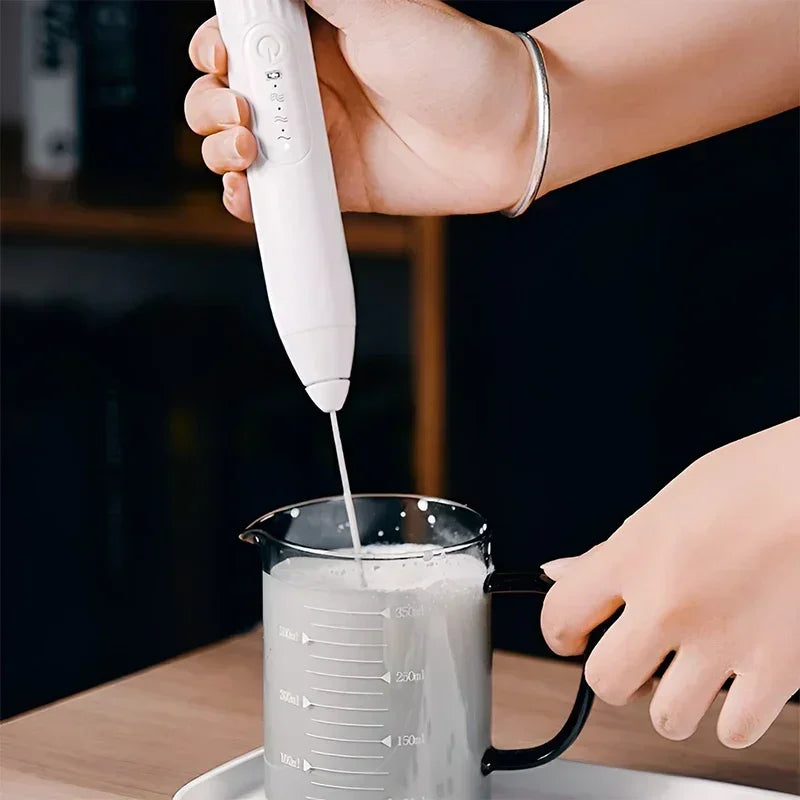 Handheld USB milk frother whisking milk in a transparent measuring cup