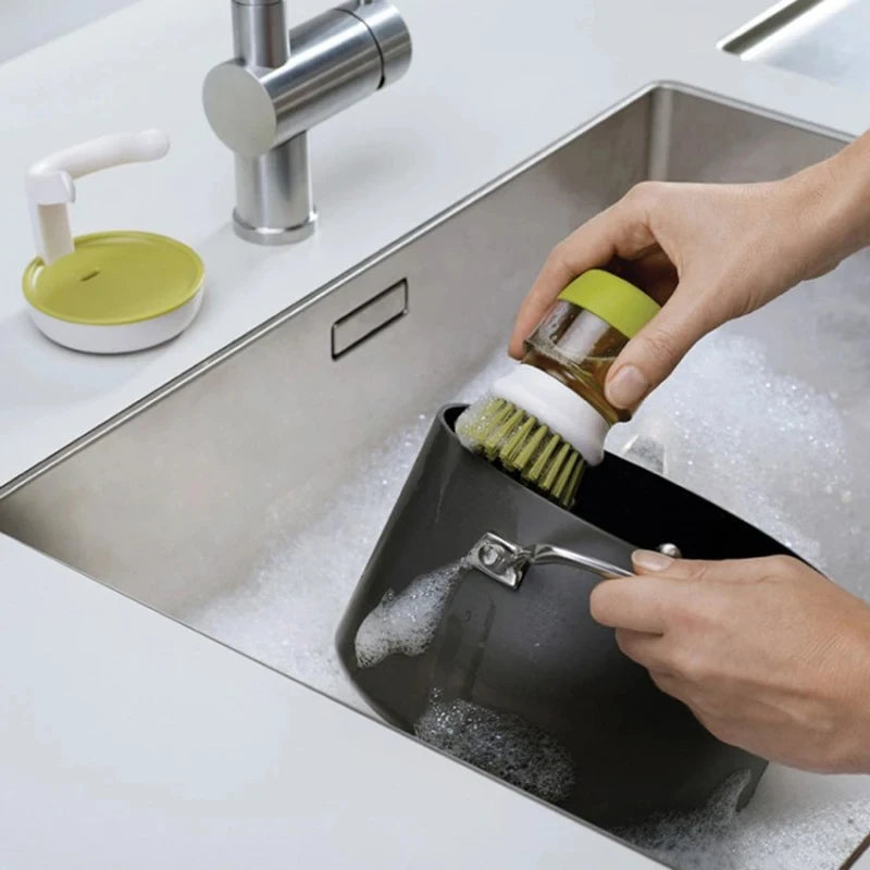 Person using a black dish brush holder with a green scrubber in a kitchen sink.