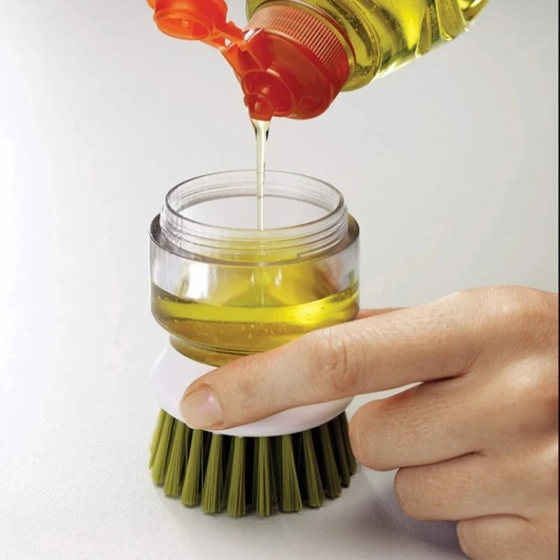 Hand pouring oil into a clear container with a green brush on a white background