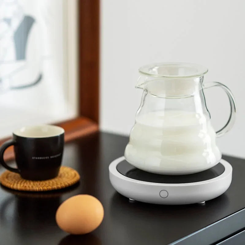 Glass milk jug on round coffee mug warmer in cozy kitchen setting