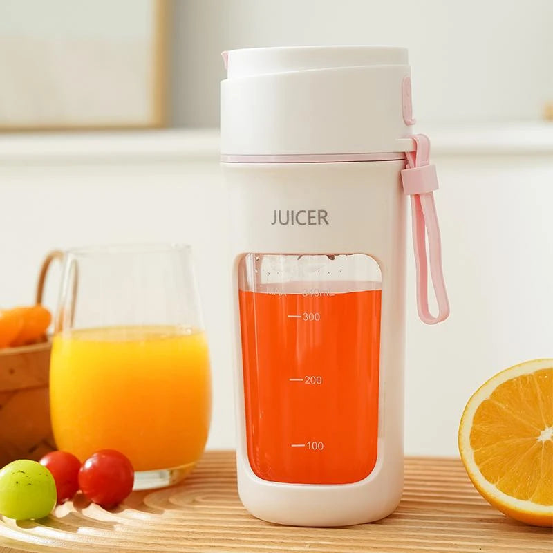 White and pink portable juicer with orange juice next to a glass of orange juice and fruits on a wooden surface.