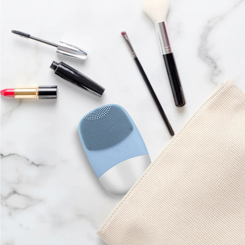 Blue silicone face cleansing brush displayed with makeup items in a travel pouch